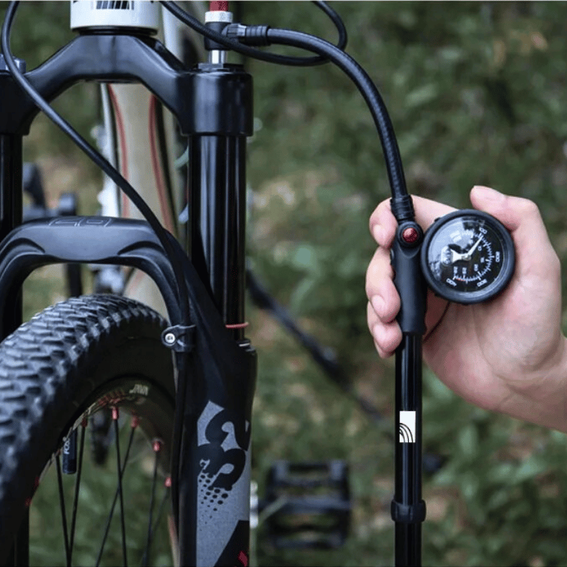 Manual shock pump in action inflating rear suspension with Schrader valve. Essential tool for mountain biking performance.

